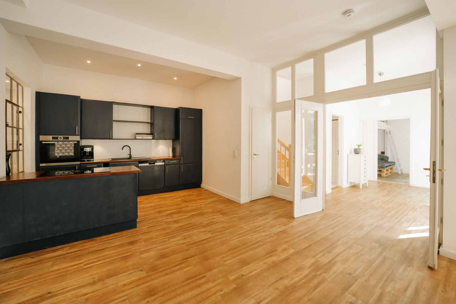 Offene moderne Küche mit dunklen Schränken und Holzfußboden in einem hellen Wohnraum.