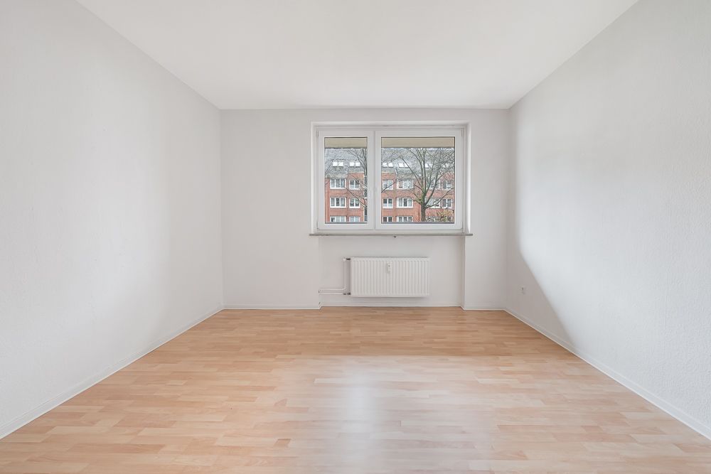 Leerer, heller Raum mit Holzfußboden, weiß gestrichenen Wänden und großem Fenster.