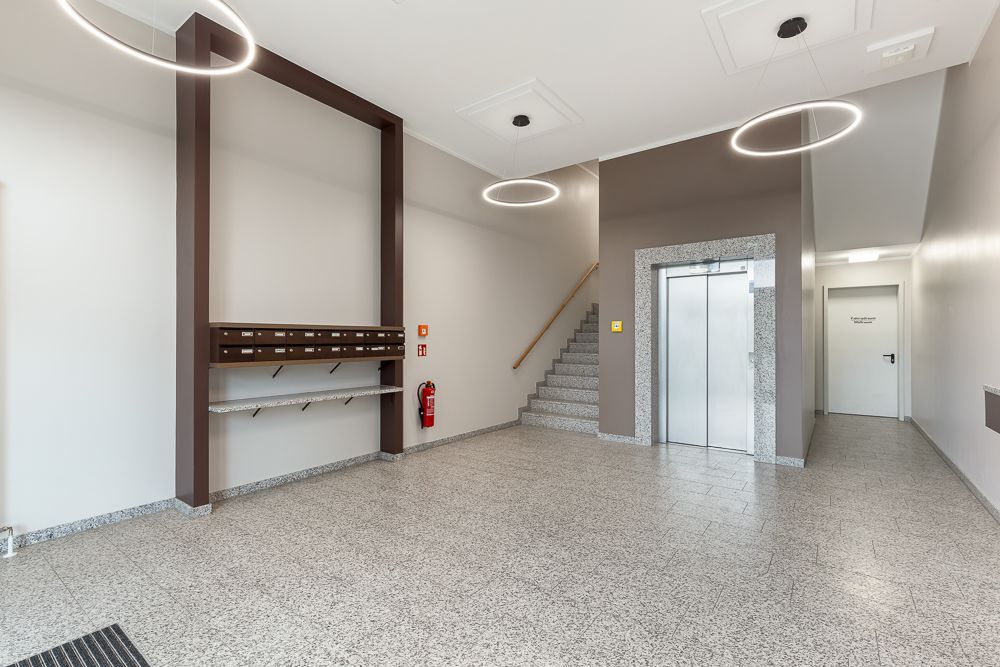 Heller Flur mit Briefkästen, Aufzug, Treppenhaus und modernen Deckenleuchten.