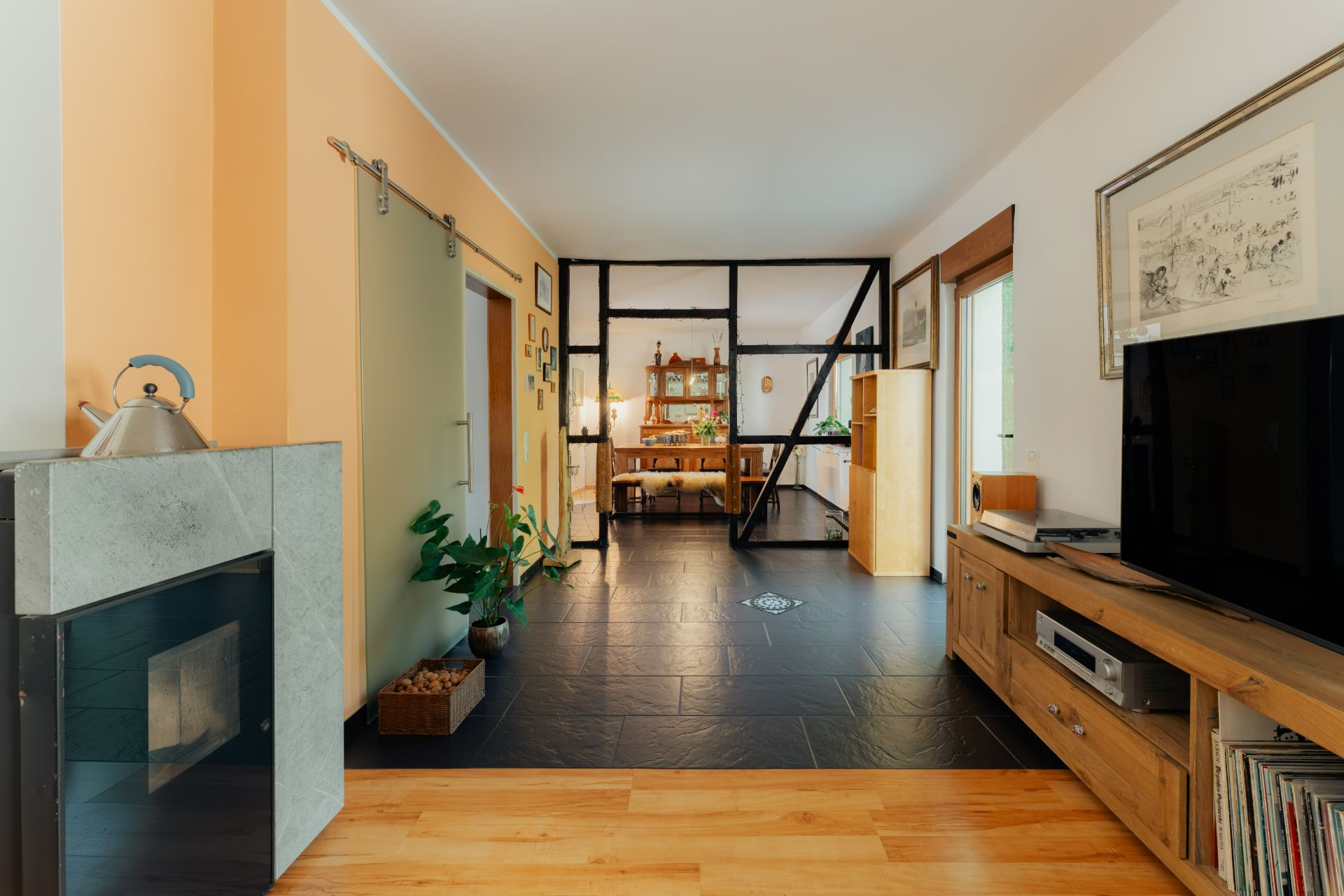 Modernes Wohnzimmer mit Kamin, Fernseher und Blick auf Essbereich mit Pflanzen.