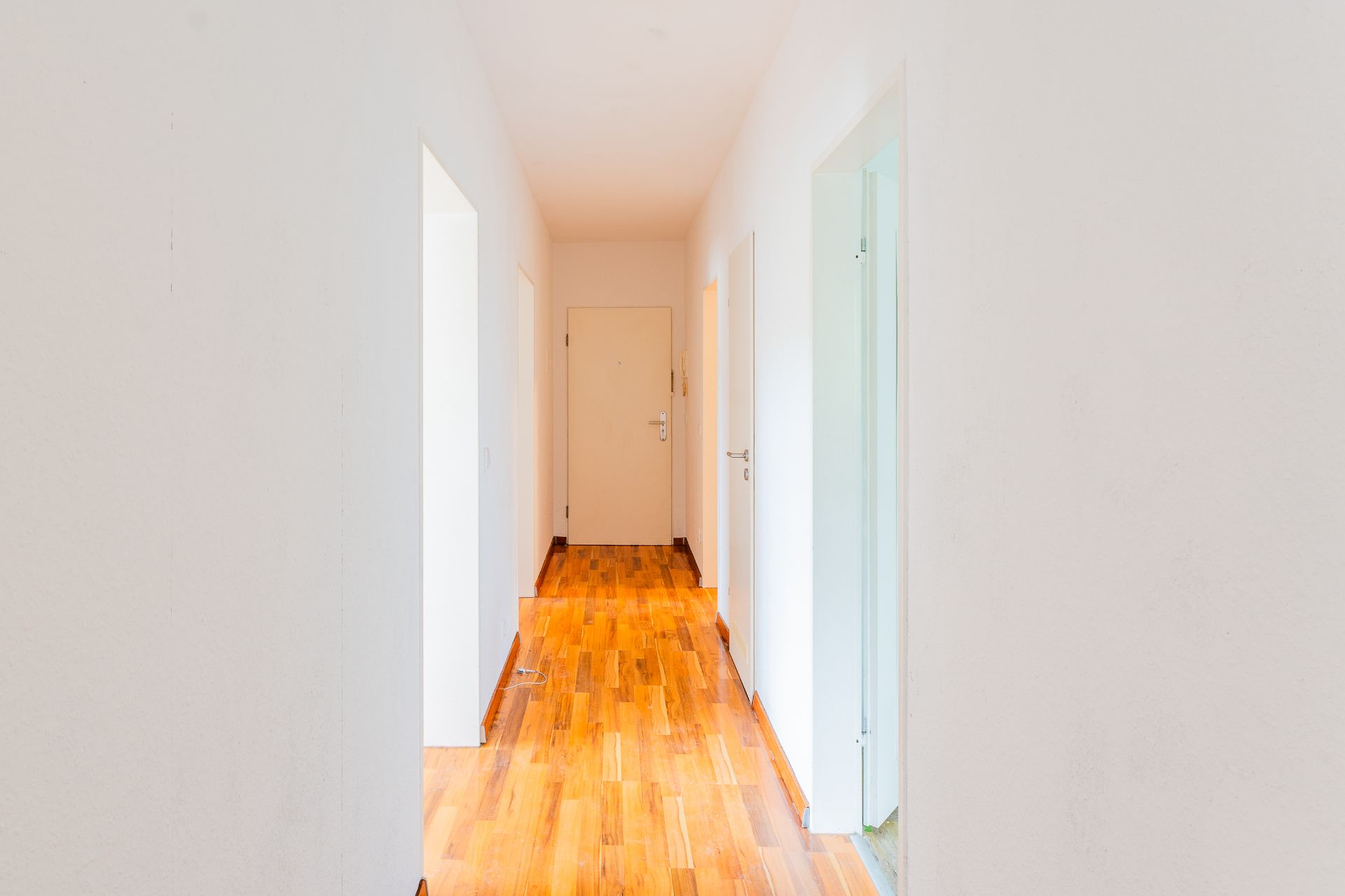 Heller Flur mit weißen Wänden und Holzboden, mehrere Türen führen in andere Räume.