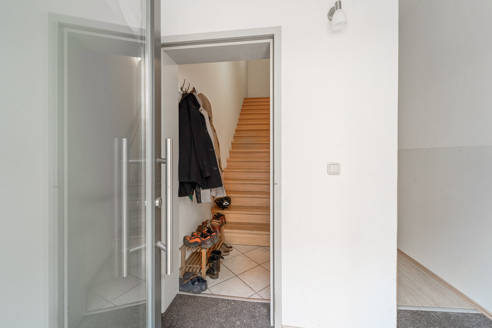 Eingangsbereich mit offener Tür, Garderobe, Schuhregal und Treppe nach oben.