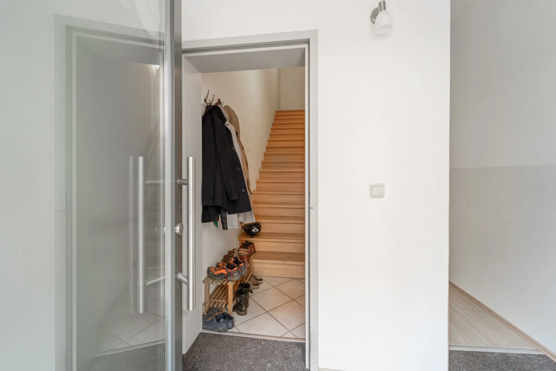 Eingangsbereich mit offener Tür, Garderobe, Schuhregal und Treppe nach oben.
