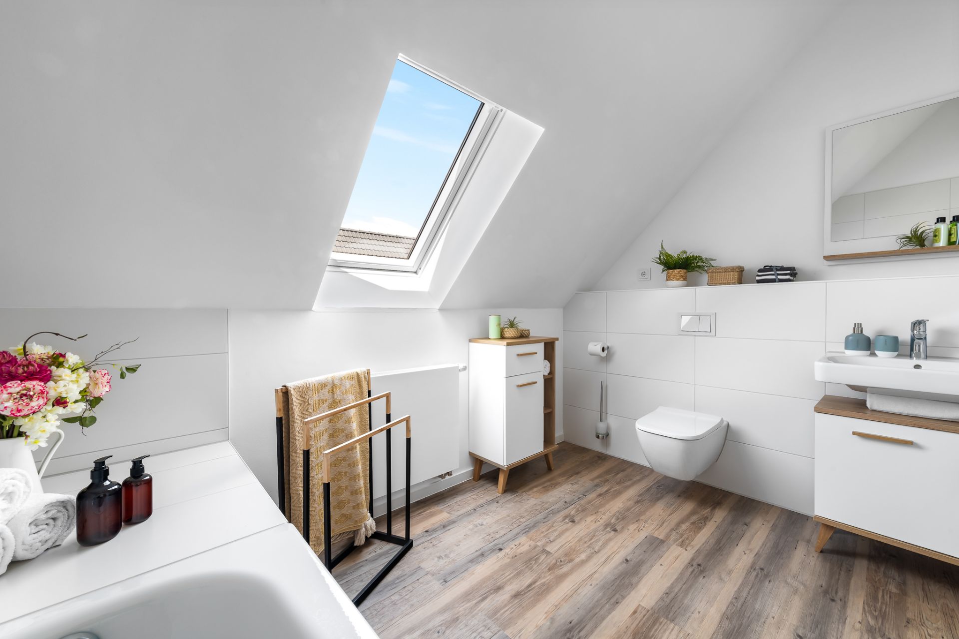 Modernes Badezimmer mit Dachfenster, Badewanne, Waschbecken und Holzfußboden.