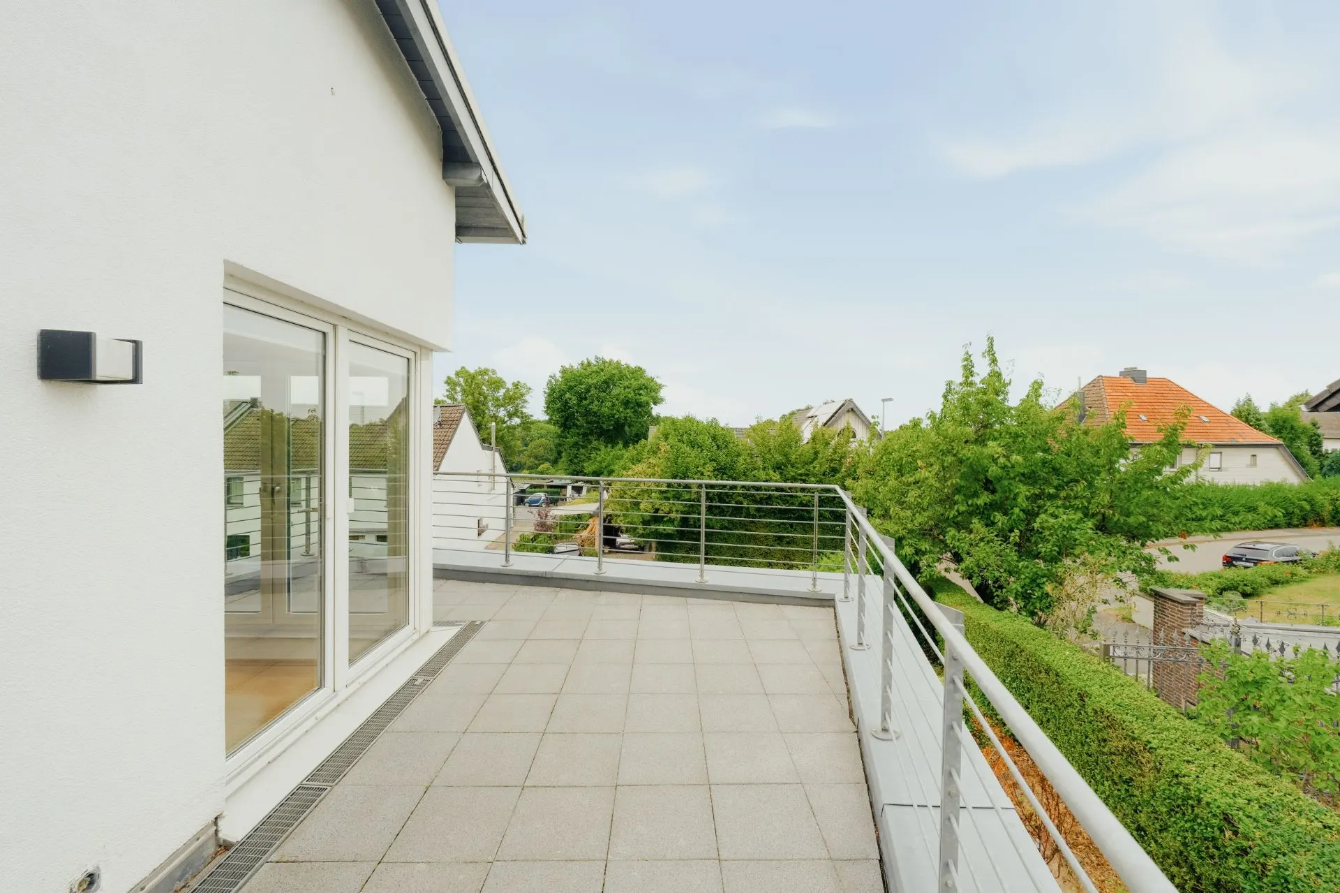 Große Dachterrasse mit Fliesenboden, Geländer und Blick auf Nachbarhäuser und Grünflächen.