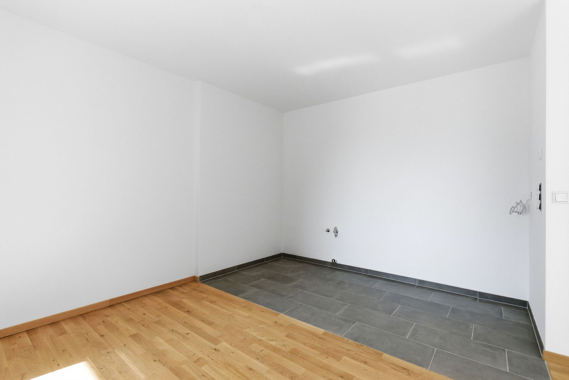 Leerer Raum mit Holzboden und einer Ecke mit dunklem Fliesenboden.