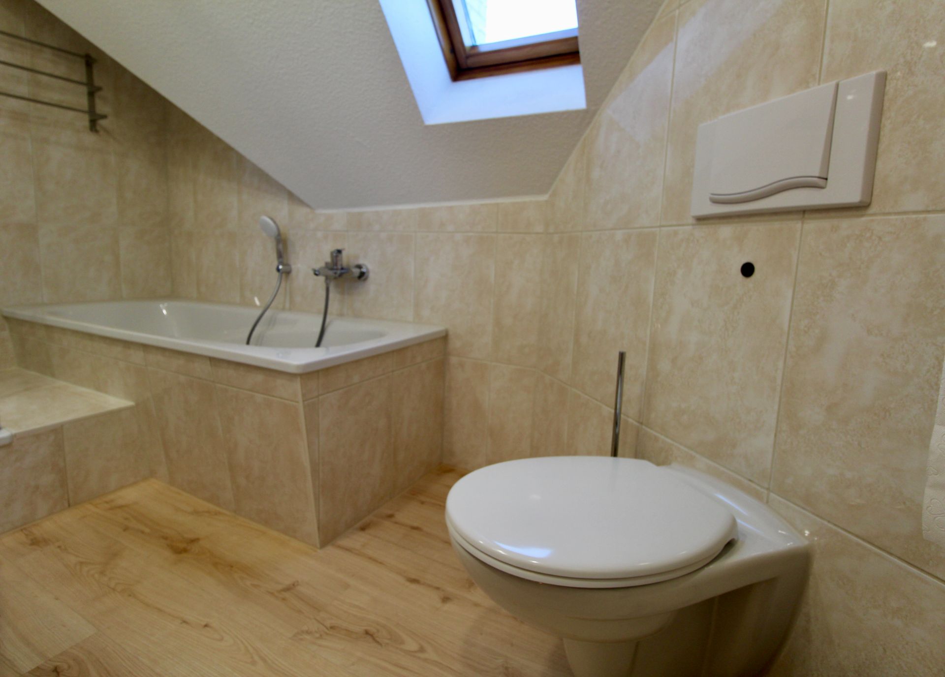 Modernes Badezimmer mit Badewanne, Toilette und Dachfenster unter einer Schräge.