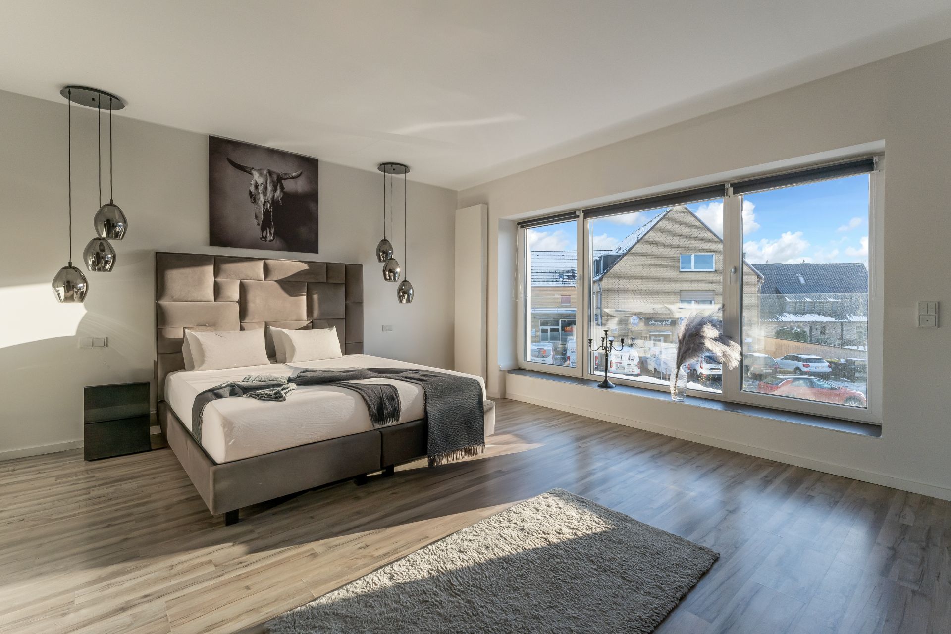 Modernes Schlafzimmer mit großem Bett, Hängelampen und großem Fenster mit Blick nach draußen.
