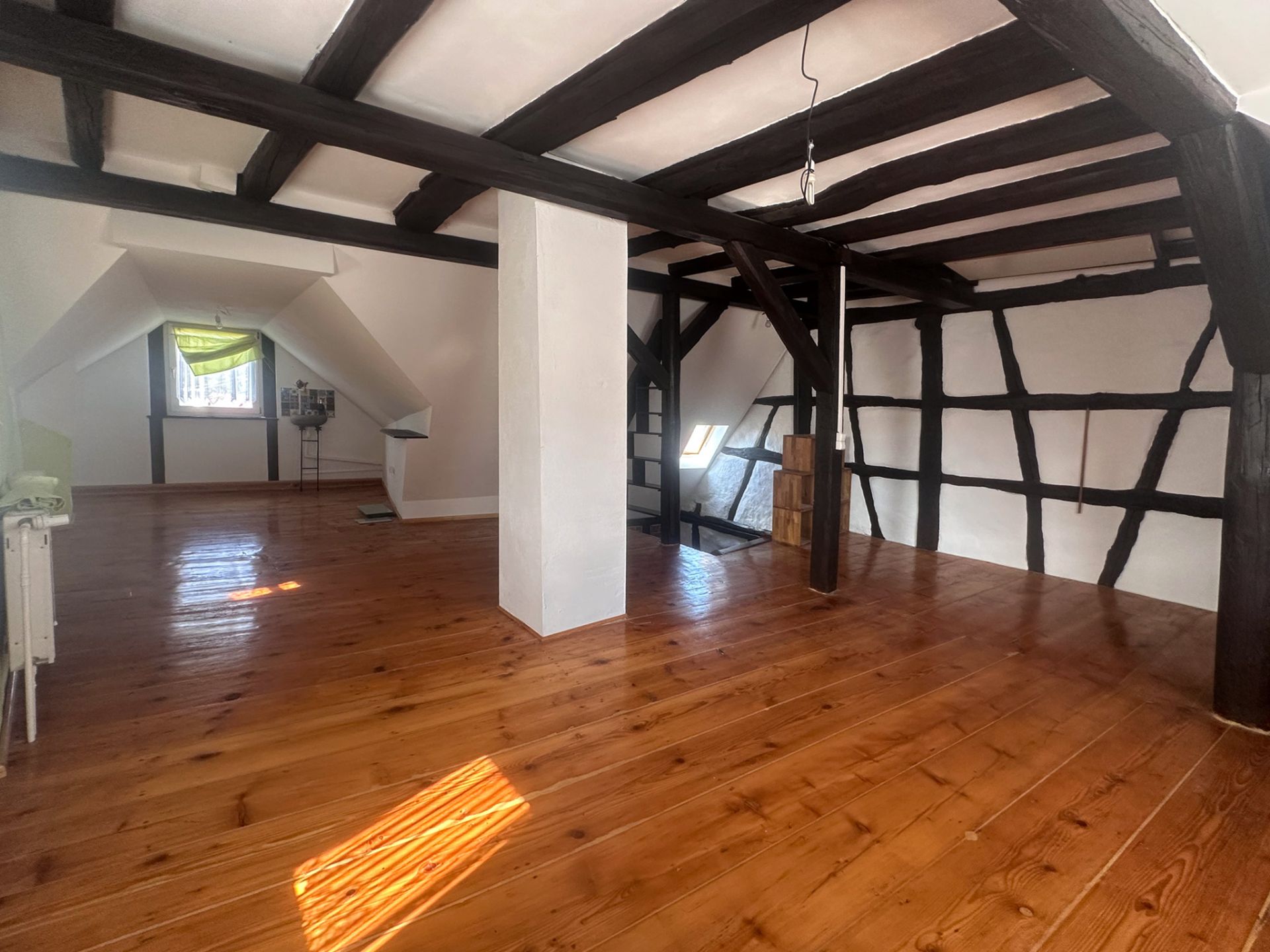 Heller Dachbodenraum mit Holzboden und sichtbaren dunklen Holzbalken.