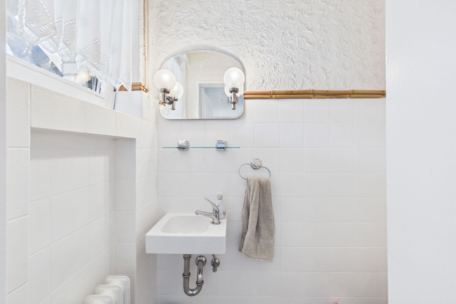 Kleines Badezimmer mit Waschbecken, Spiegel, Handtuch und Fenster mit Vorhang.