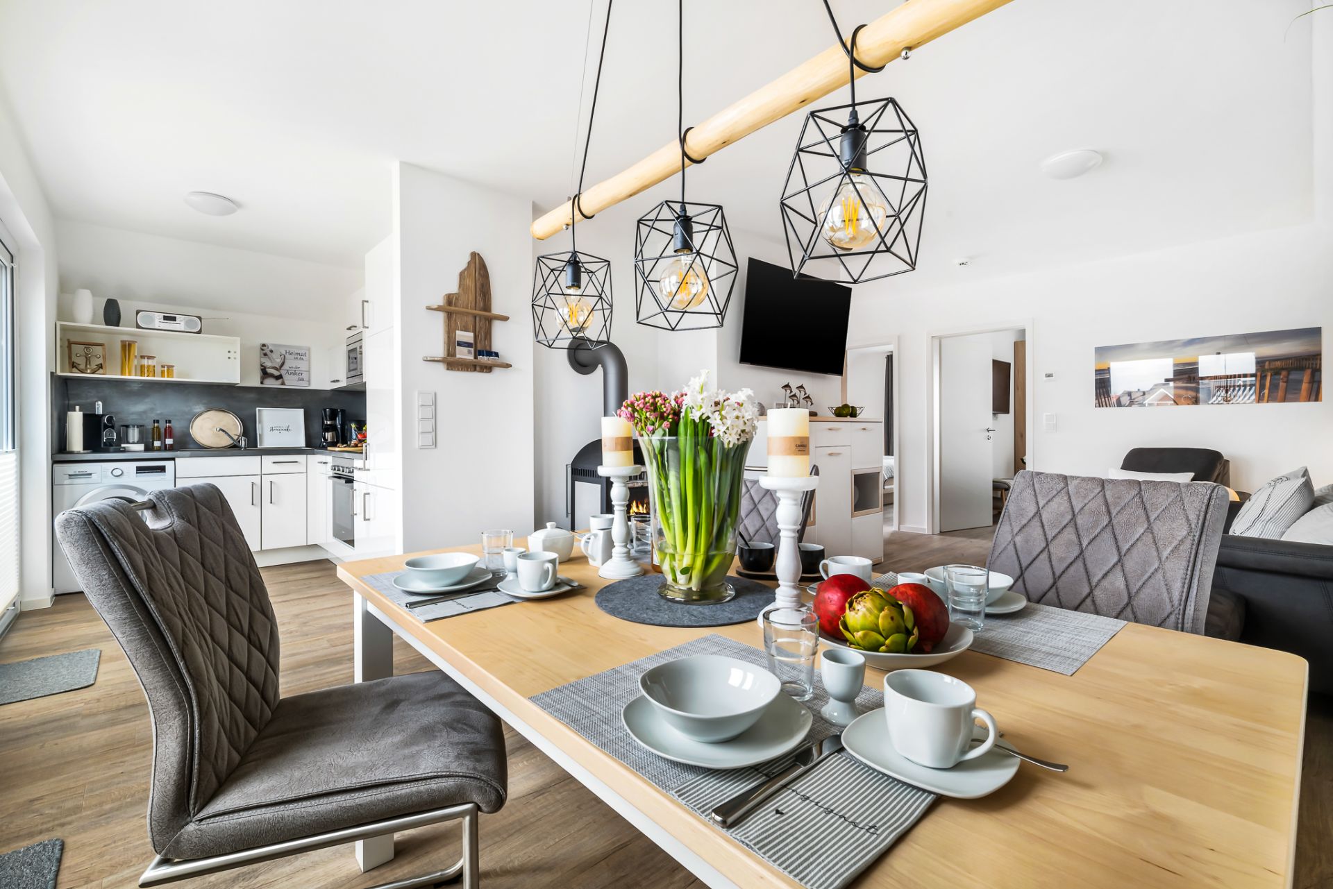Modern eingerichtetes Esszimmer mit gedecktem Tisch und offener Küche im Hintergrund.