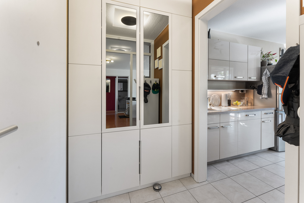 Eingangsbereich mit großem weißen Spiegelschrank, Blick in eine helle Küche.