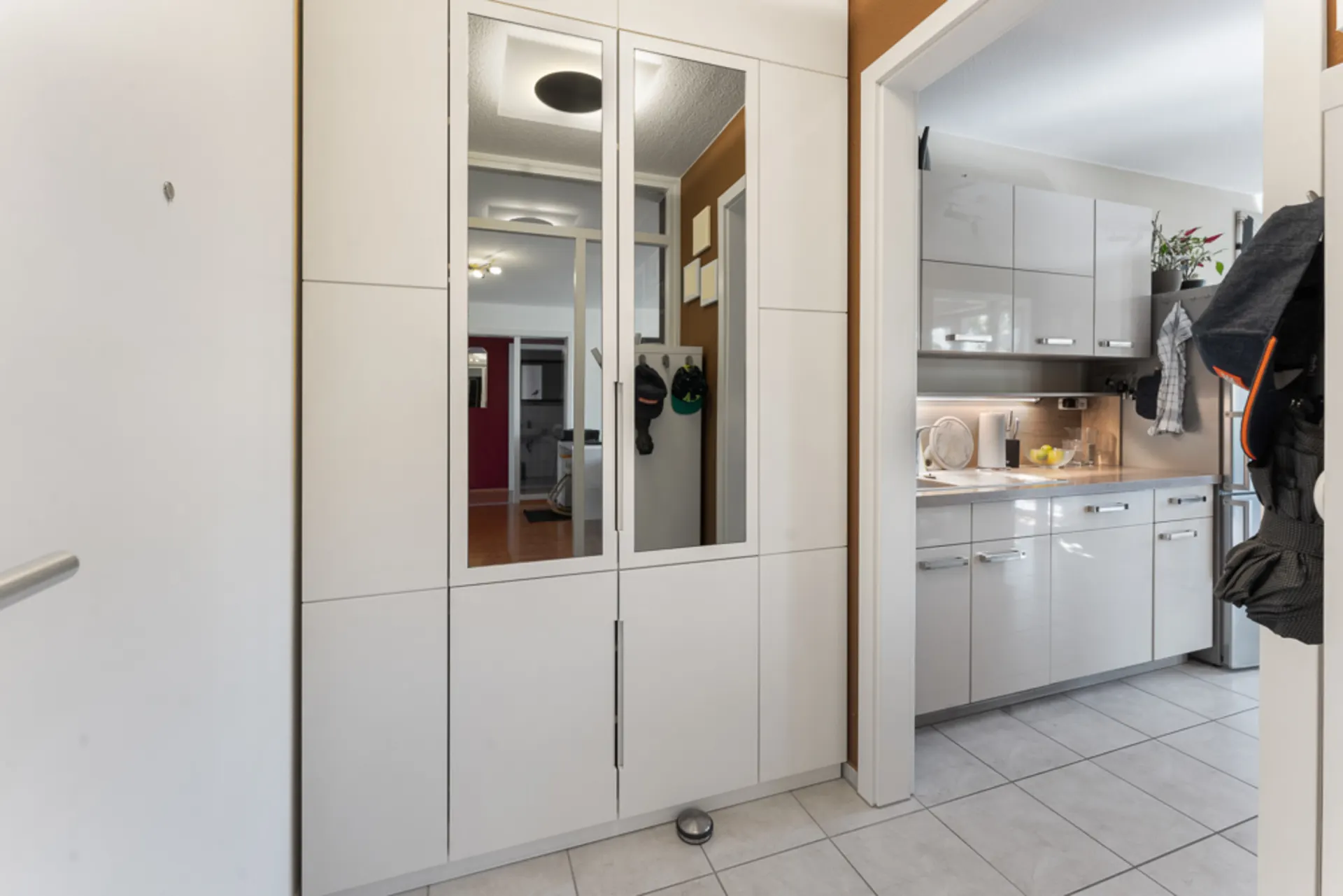 Eingangsbereich mit großem weißen Spiegelschrank, Blick in eine helle Küche.