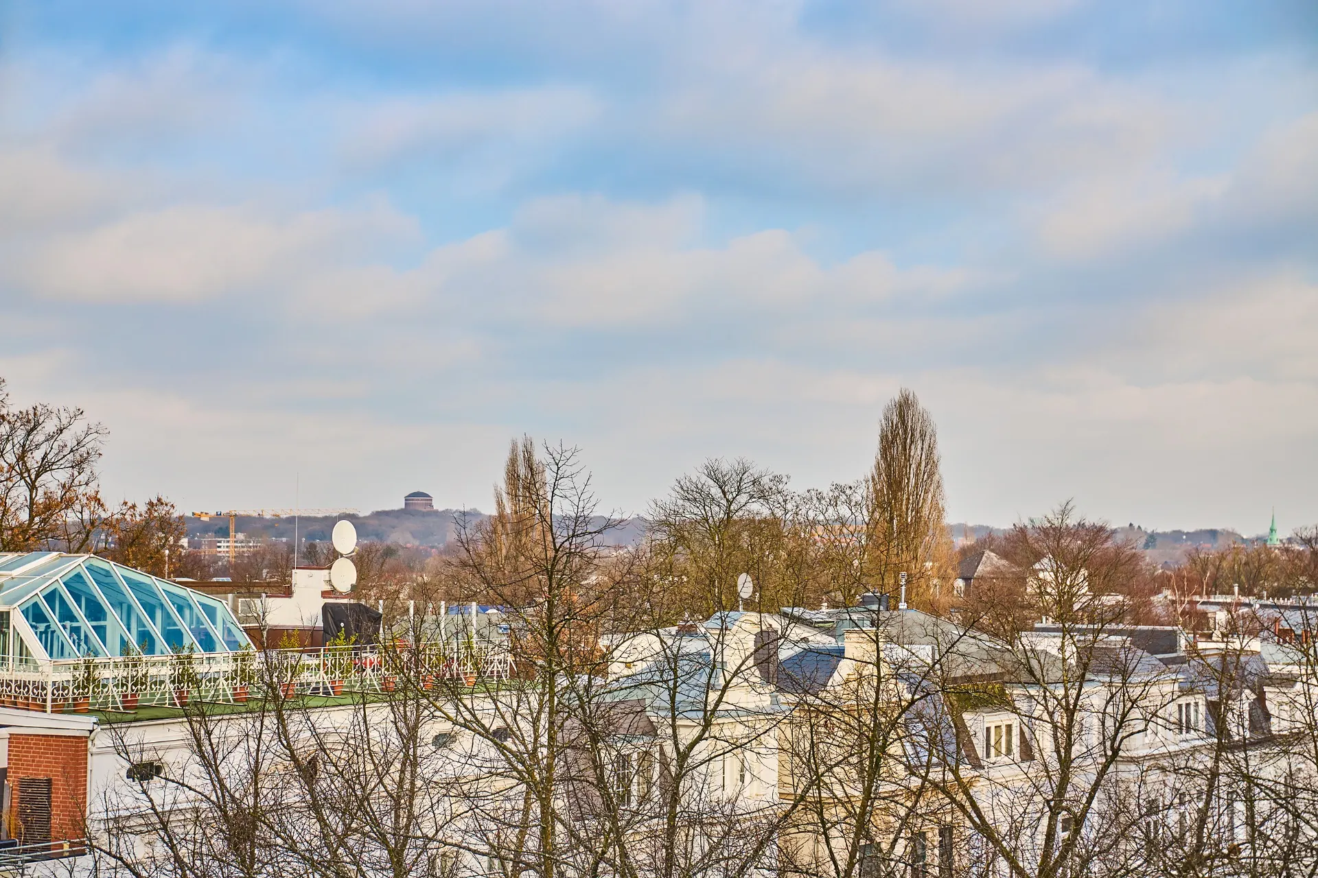 Blick über Dächer und Bäume einer Wohngegend bei bewölktem Himmel.