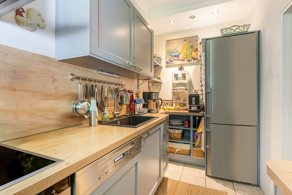 Moderne Wohnküche mit grauen Schränken, Holzarbeitsplatte und großem Kühlschrank.