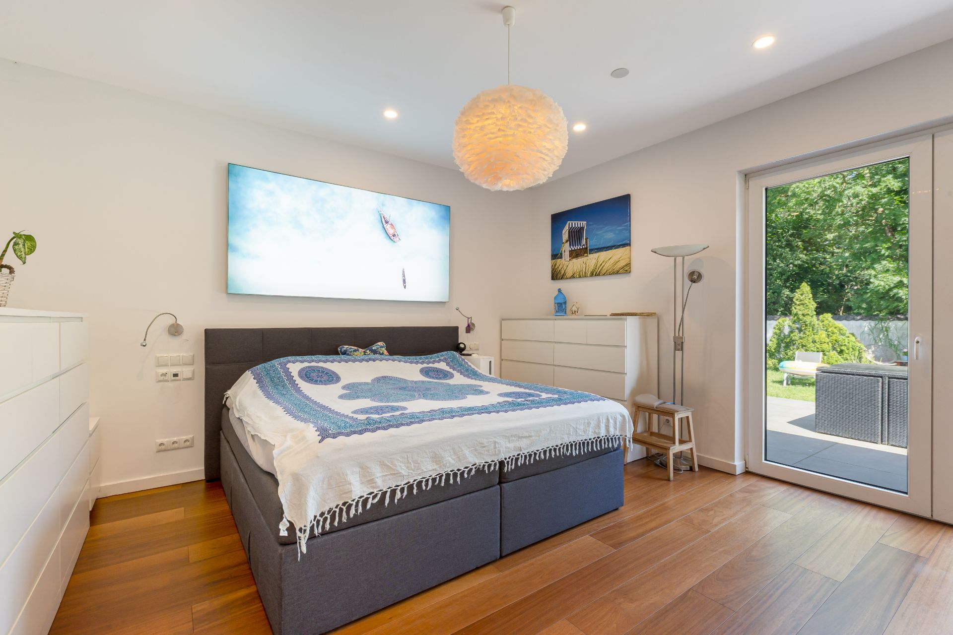 Helles Schlafzimmer mit Doppelbett, Holzfußboden, Kommoden und Zugang zur Terrasse.