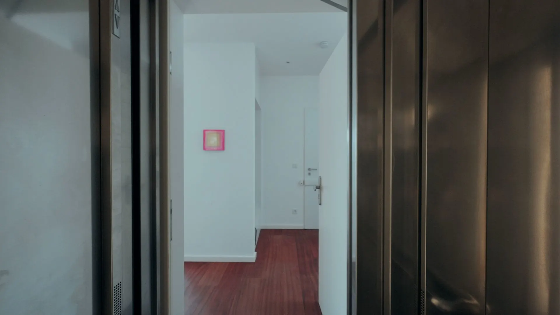 Blick aus einem Aufzug in einen Flur einer Wohnung mit Holzboden und weißer Wand.