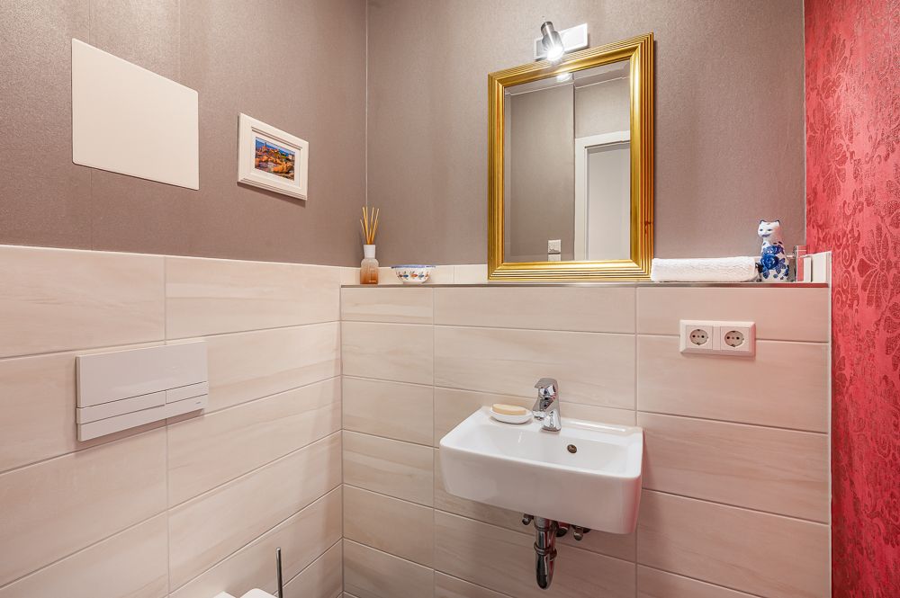 Kleines Badezimmer mit Waschbecken, Spiegel mit goldenem Rahmen und Wanddekoration.
