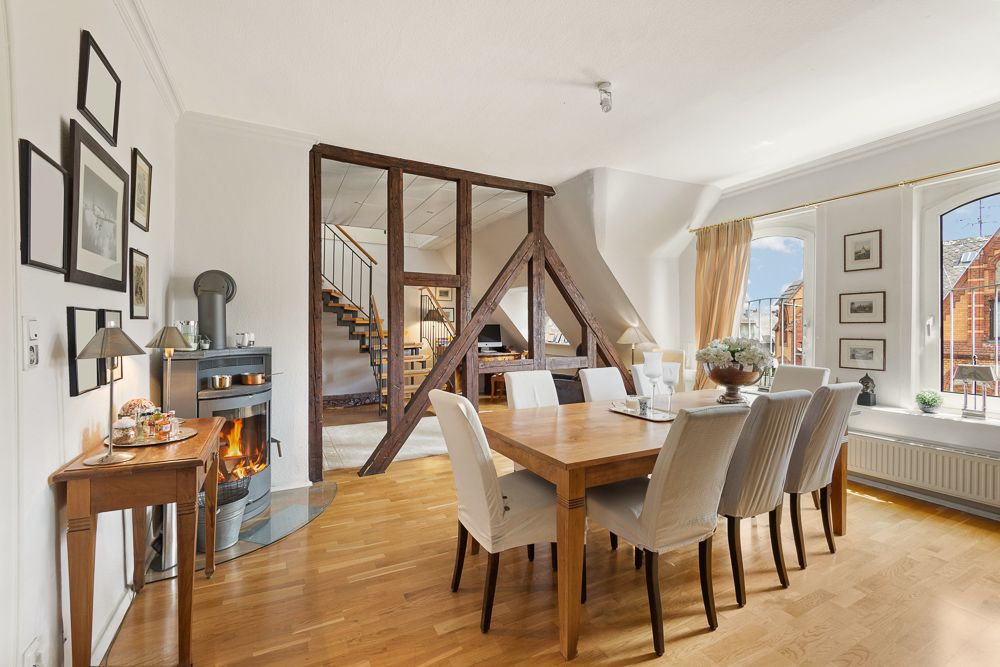 Helles Esszimmer mit großem Holztisch, Kamin und sichtbaren Holzbalken im Hintergrund.