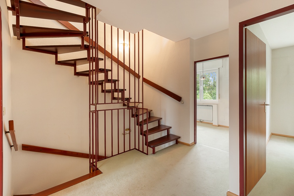 Eine Holzwendeltreppe in einem Flur, daneben Türen zu weiteren Zimmern.
