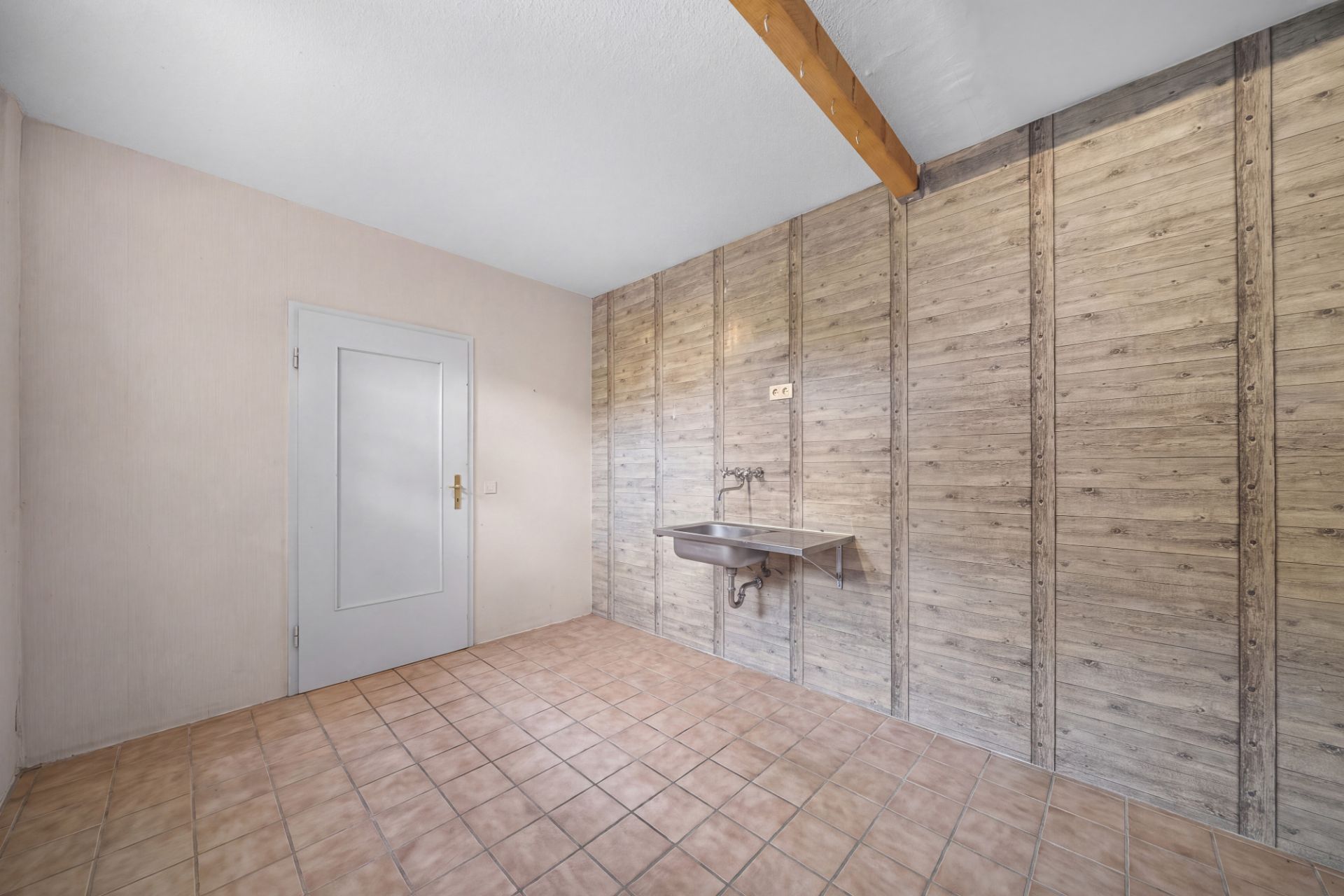 Leerer Raum mit Fliesenboden, Holzvertäfelung an der Wand und einem Wandwaschbecken.