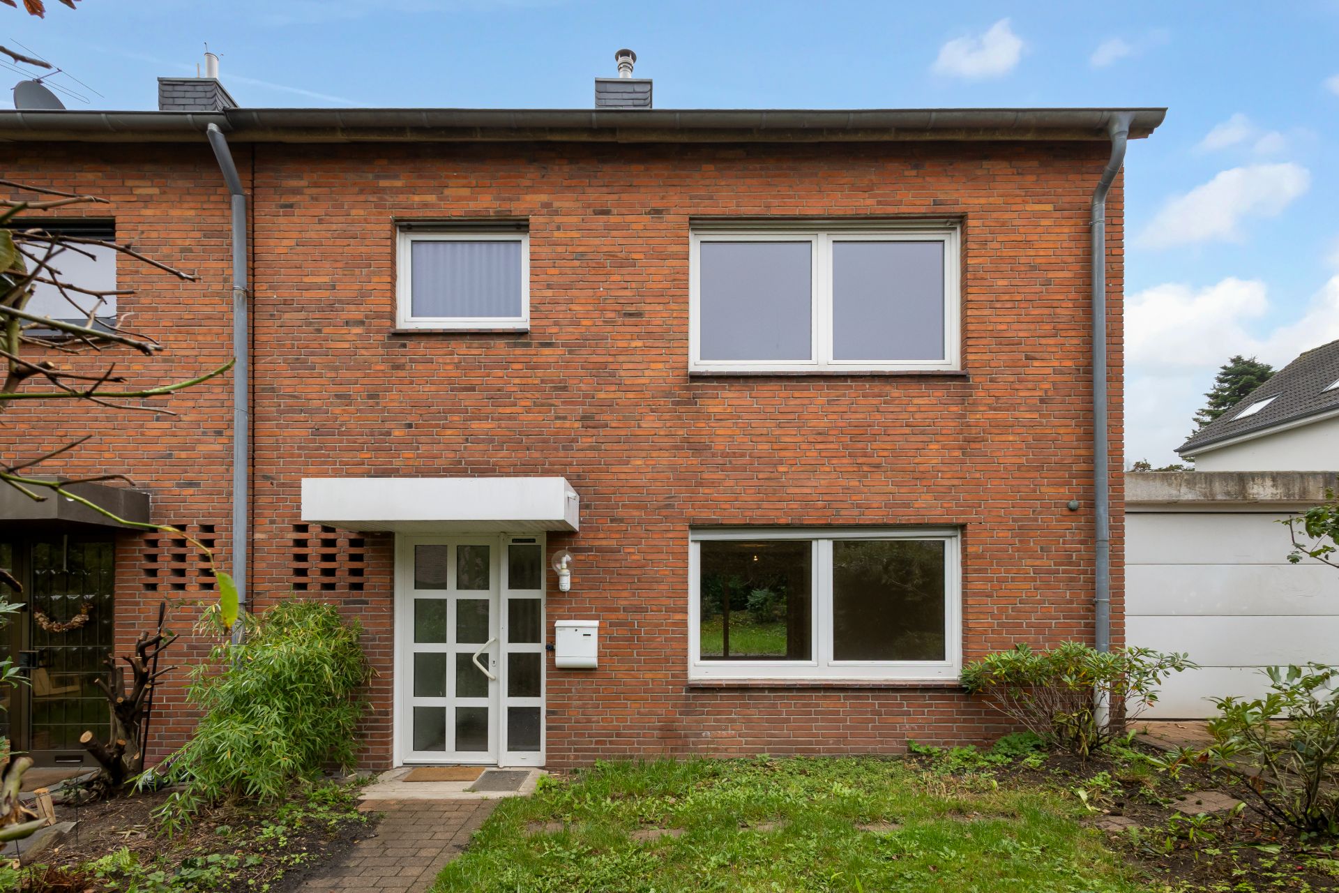 Zweistöckiges Haus aus rotem Backstein mit weißer Eingangstür und großen Fenstern, davor Rasenfläche.
