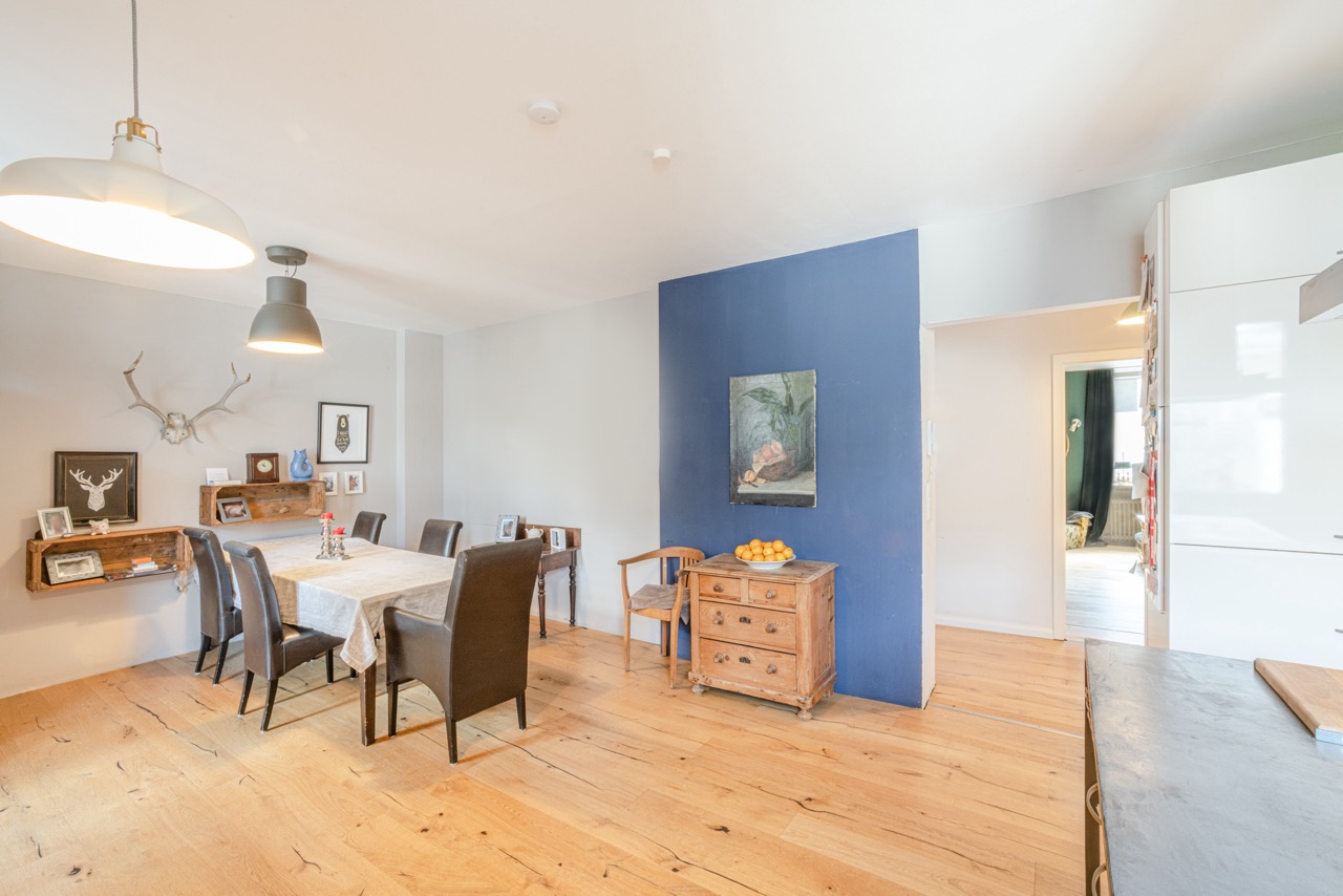 Heller Essbereich mit Holztisch, sechs Stühlen und blauer Akzentwand in einer Wohnung.