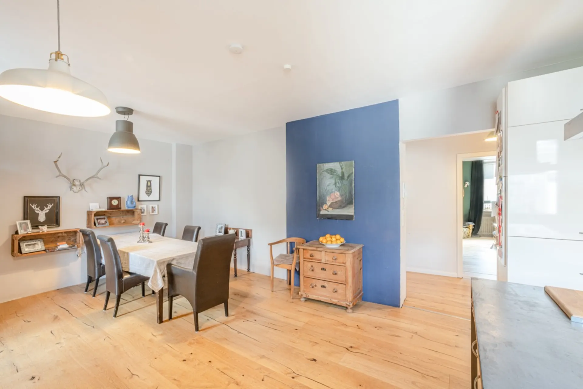Heller Essbereich mit Holztisch, sechs Stühlen und blauer Akzentwand in einer Wohnung.