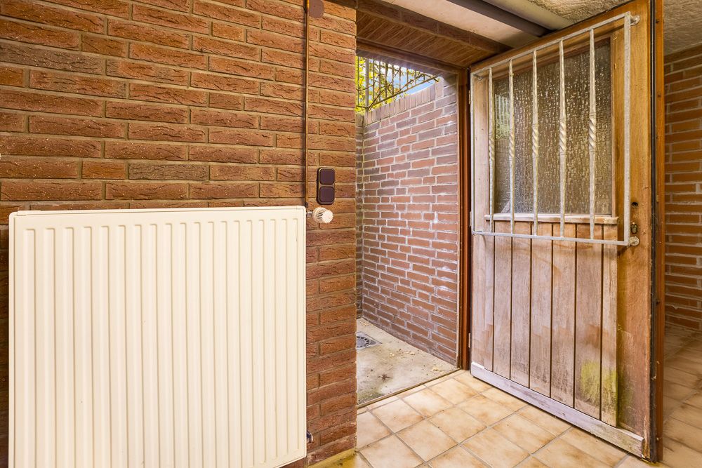 Offene Tür aus Holz mit Gitter, daneben eine Heizkörper an einer Backsteinwand.