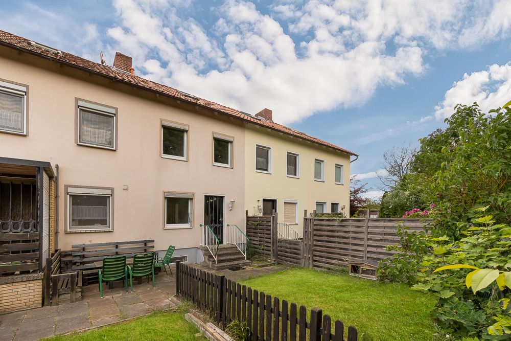 Reihenhaus mit Garten, Terrasse, Holzzaun und Gartenmöbeln im Vordergrund.