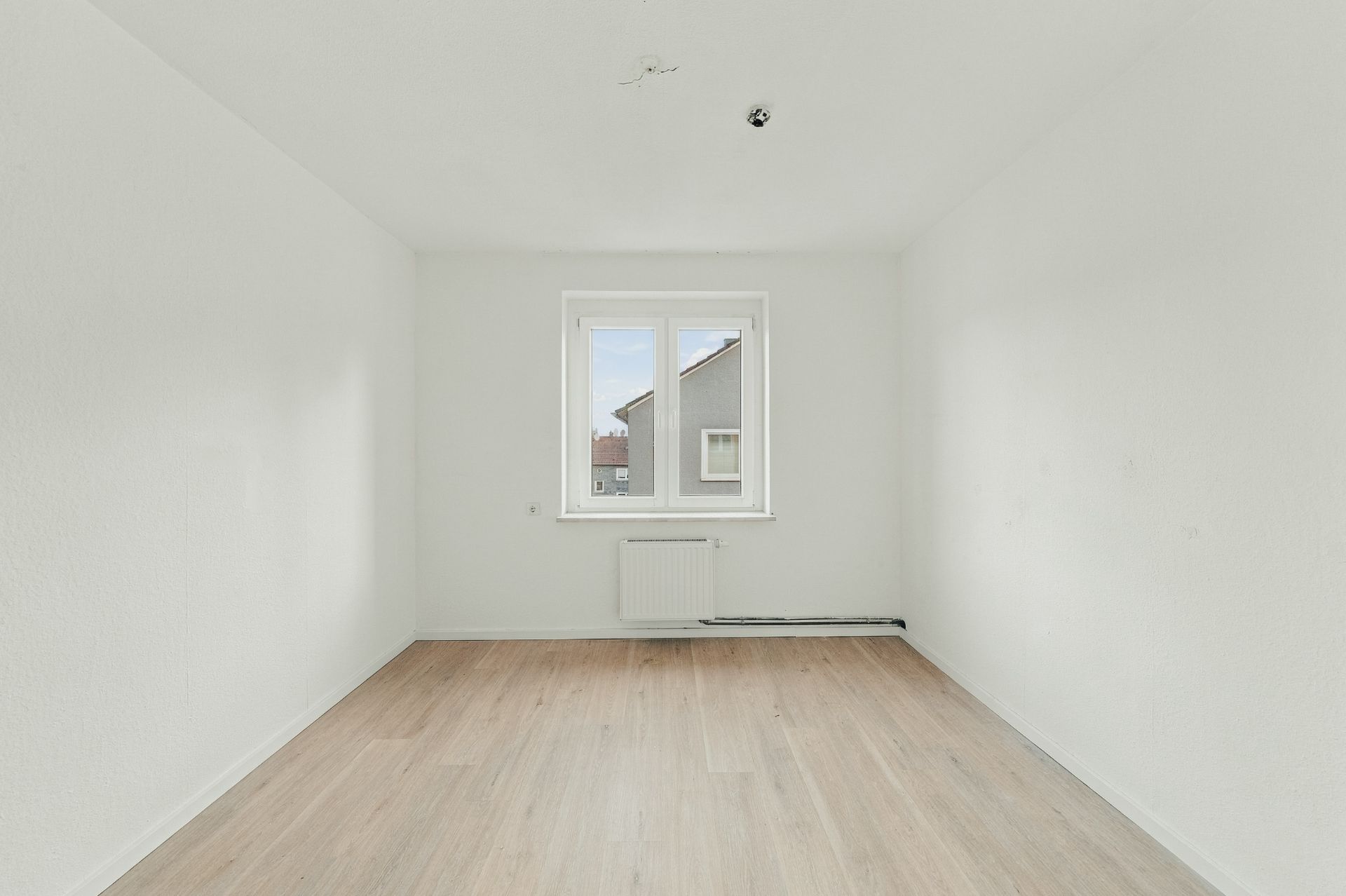 Leerer, heller Raum mit weißem Wänden, Fenster und hellem Holzboden.