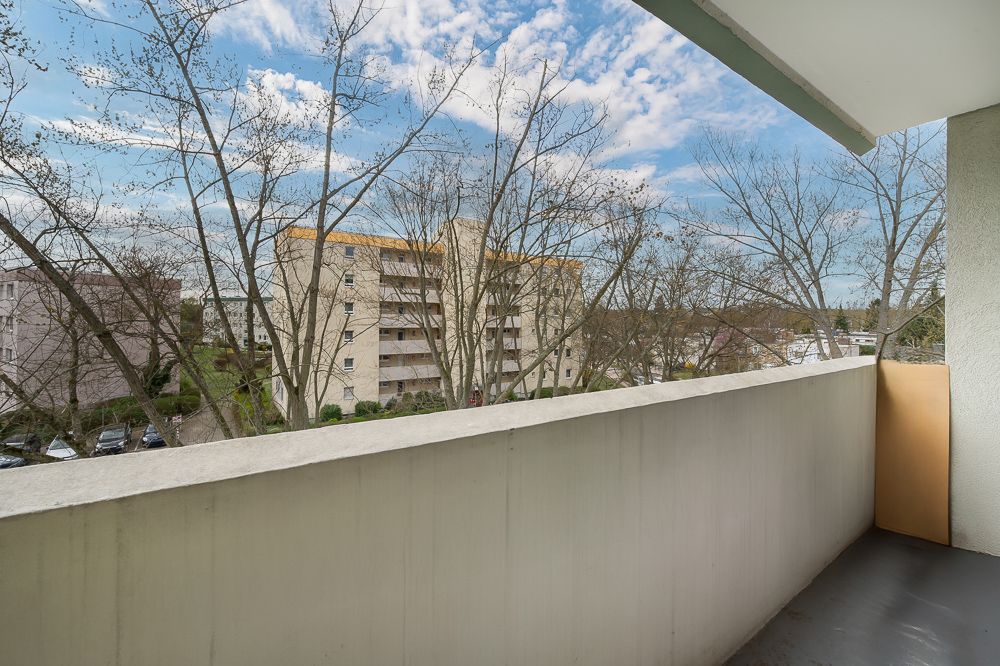 Balkon mit Blick auf Wohngebäude und Bäume bei bewölktem Himmel.