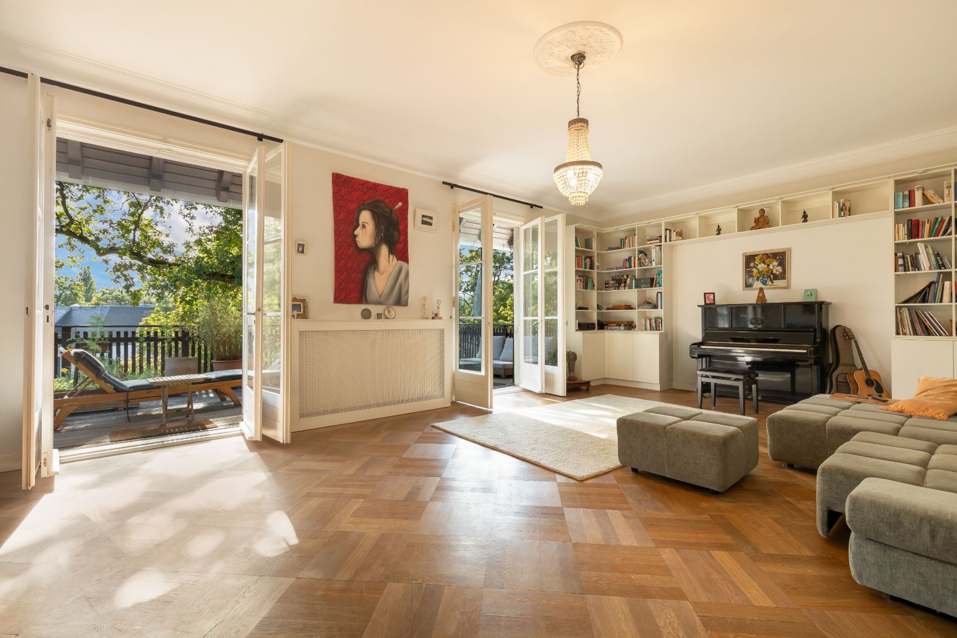 Helles Wohnzimmer mit Parkettboden, Klavier, Bücherregalen und Zugang zur Terrasse.