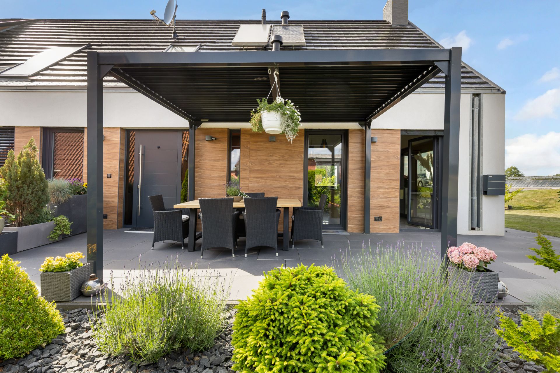 Moderne Terrasse mit Essbereich, Überdachung und Pflanzen an einem Wohnhaus.