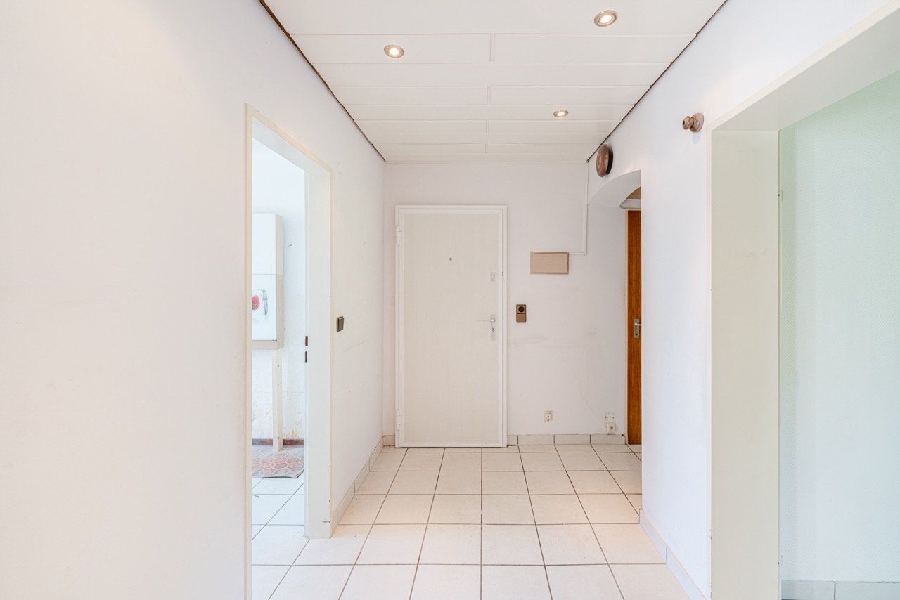 Heller Flur mit weißen Wänden, Fliesenboden und mehreren Türen in einer Wohnung.