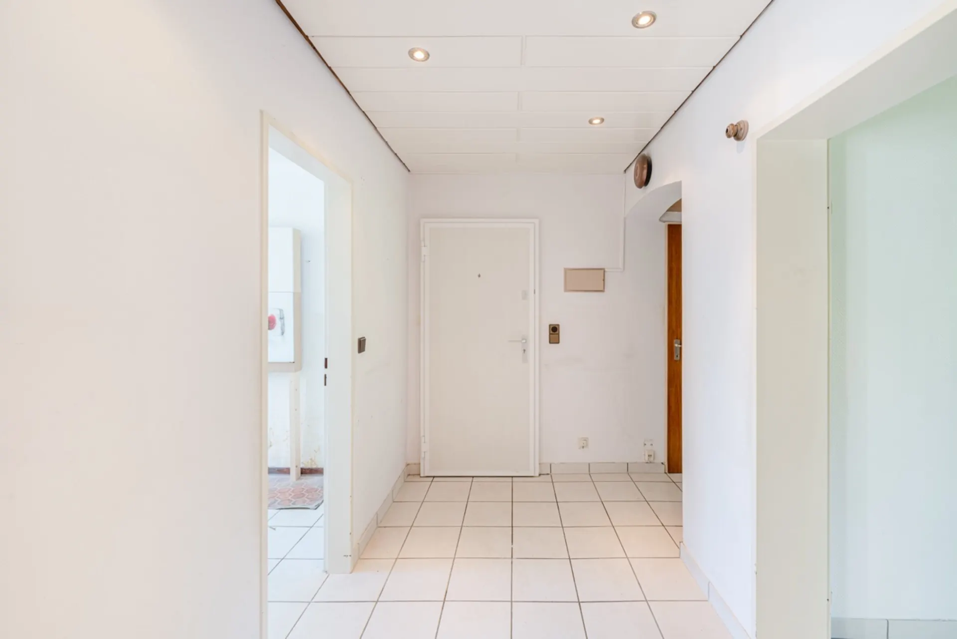 Heller Flur mit weißen Wänden, Fliesenboden und mehreren Türen in einer Wohnung.
