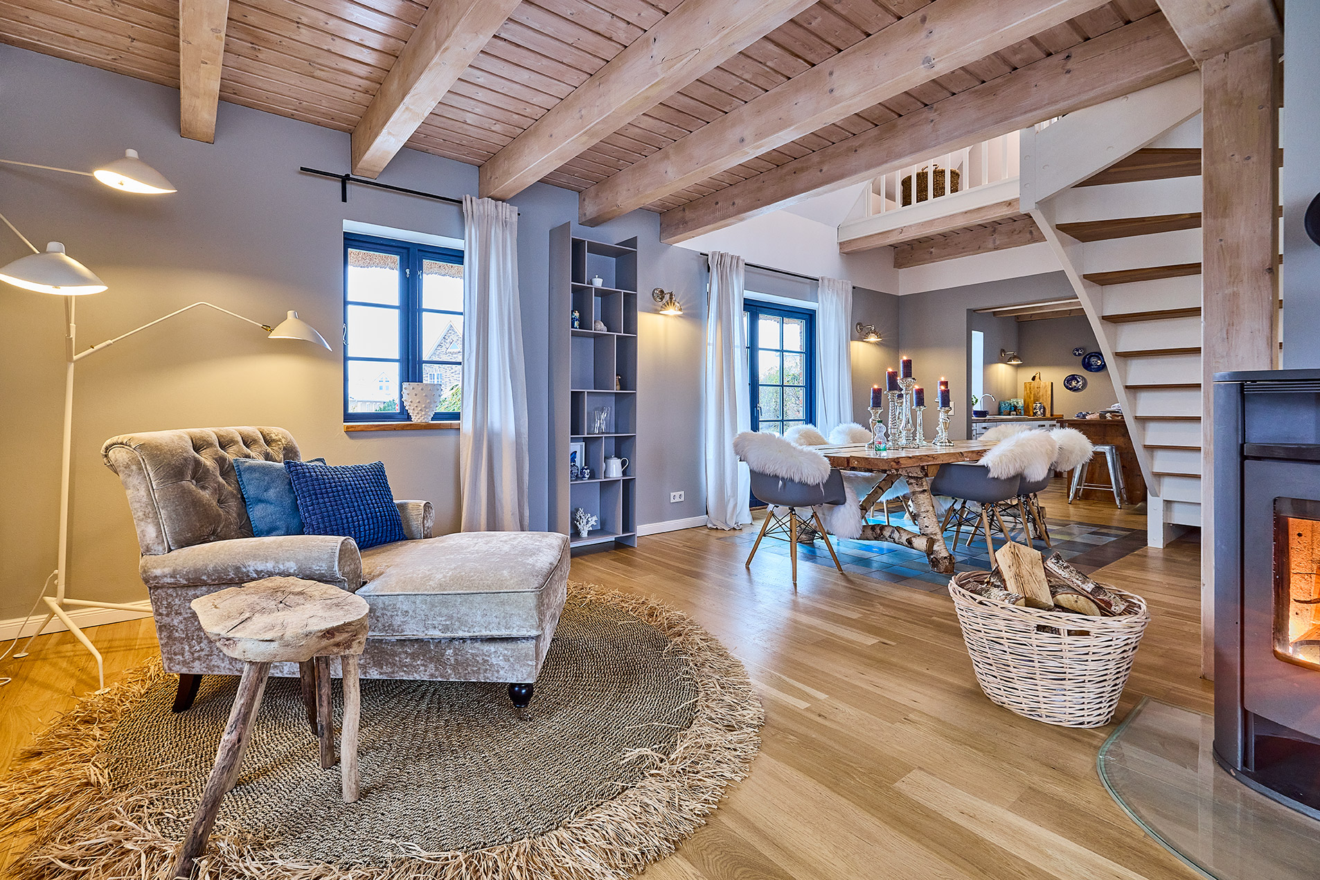 Helles Wohnzimmer mit Sessel, Holztisch, Essbereich, Kamin, Holzdecke und Treppe in modernem Stil.