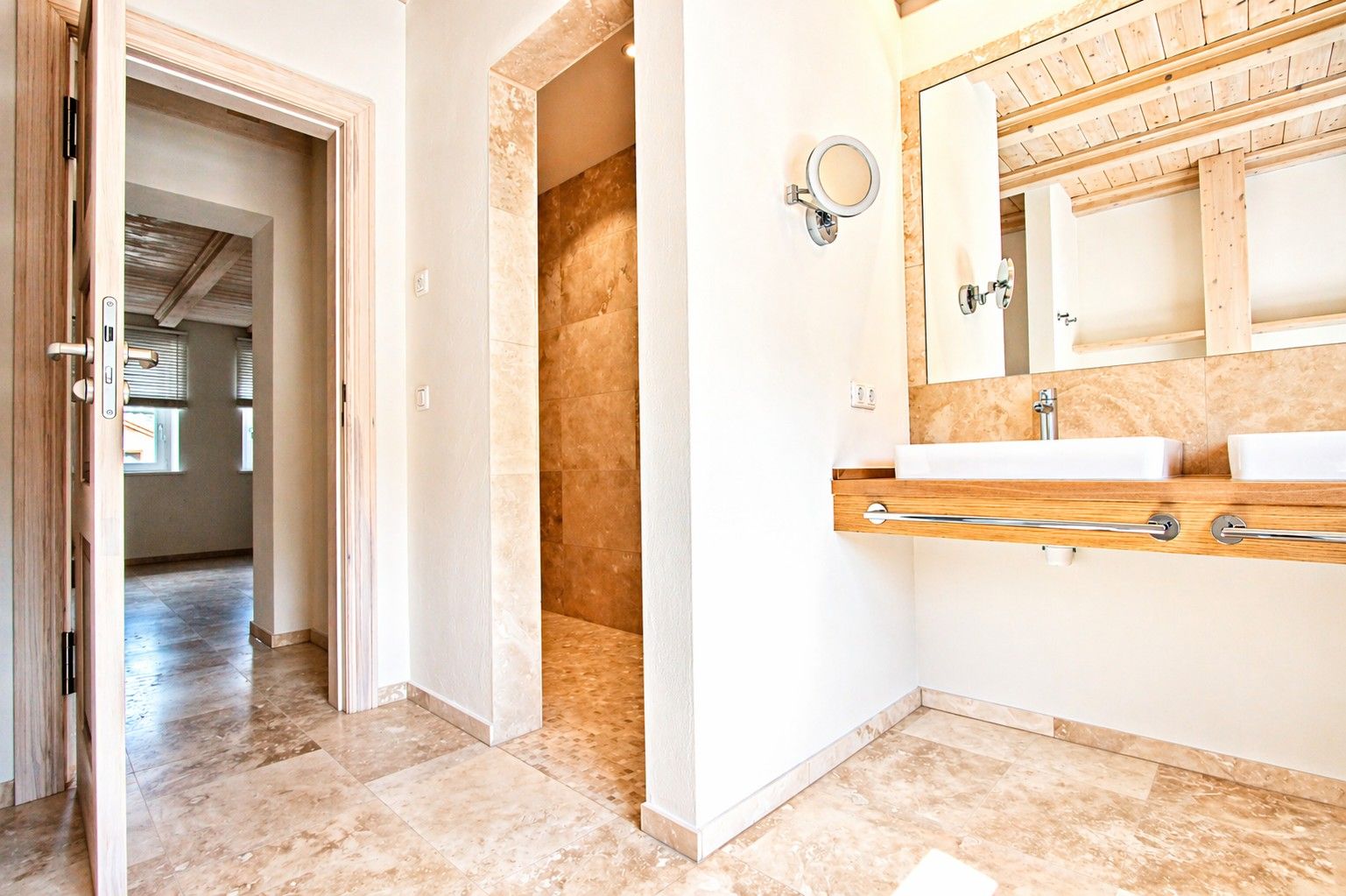 Modernes Badezimmer mit zwei Waschbecken, großem Spiegel und offener Tür zu einem hellen Raum.