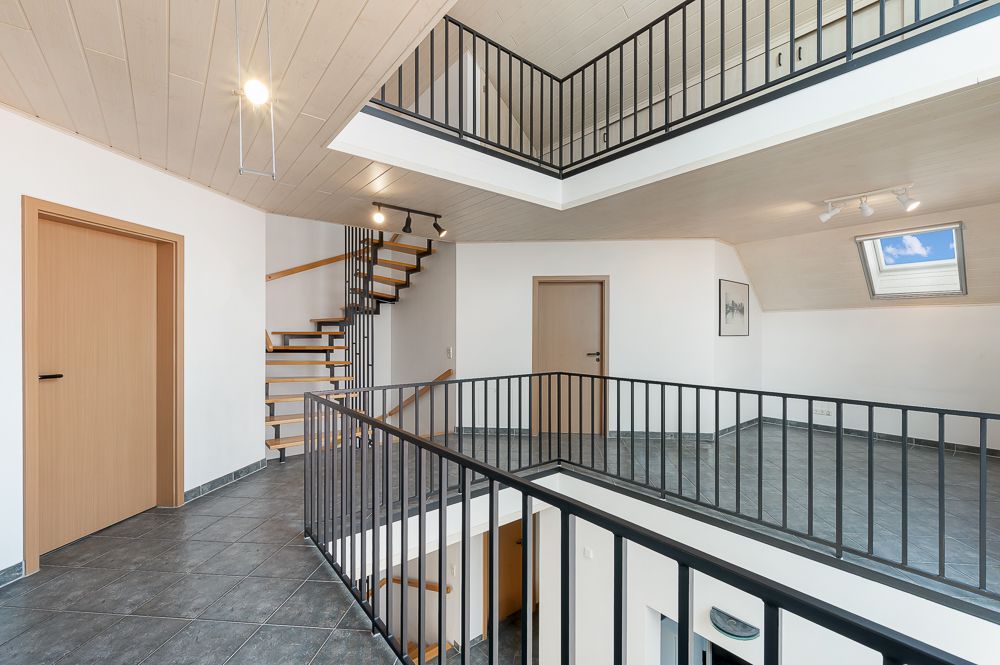 Heller Flur mit grauem Fliesenboden, zwei Holztüren, Treppe und schwarzem Geländer.