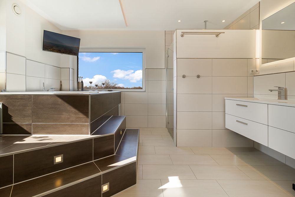 Modernes Badezimmer mit großer Badewanne, Stufen, Dusche und Wandspiegel.