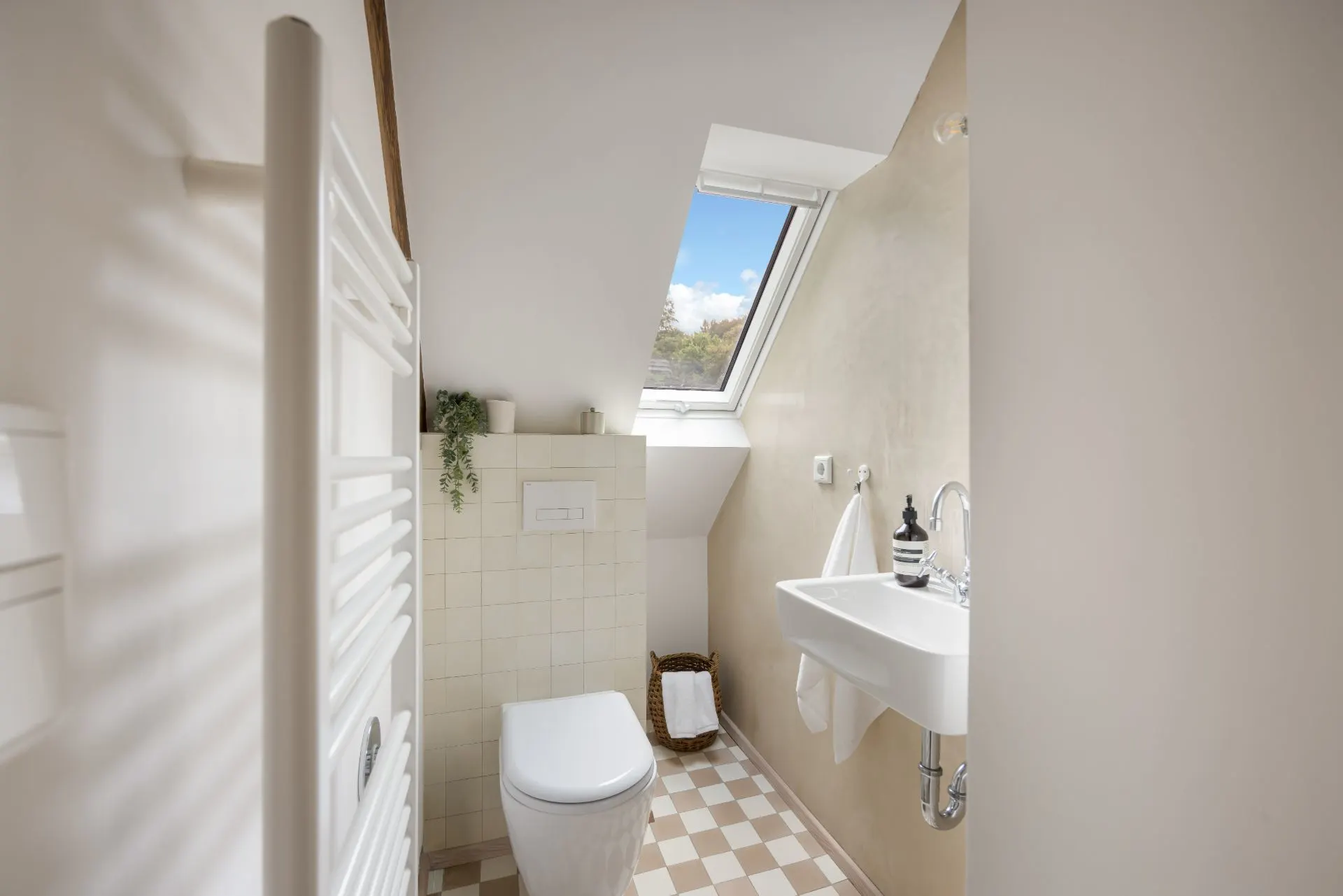 Kleines Bad mit Toilette, Waschbecken und Dachfenster unter einer Schräge.