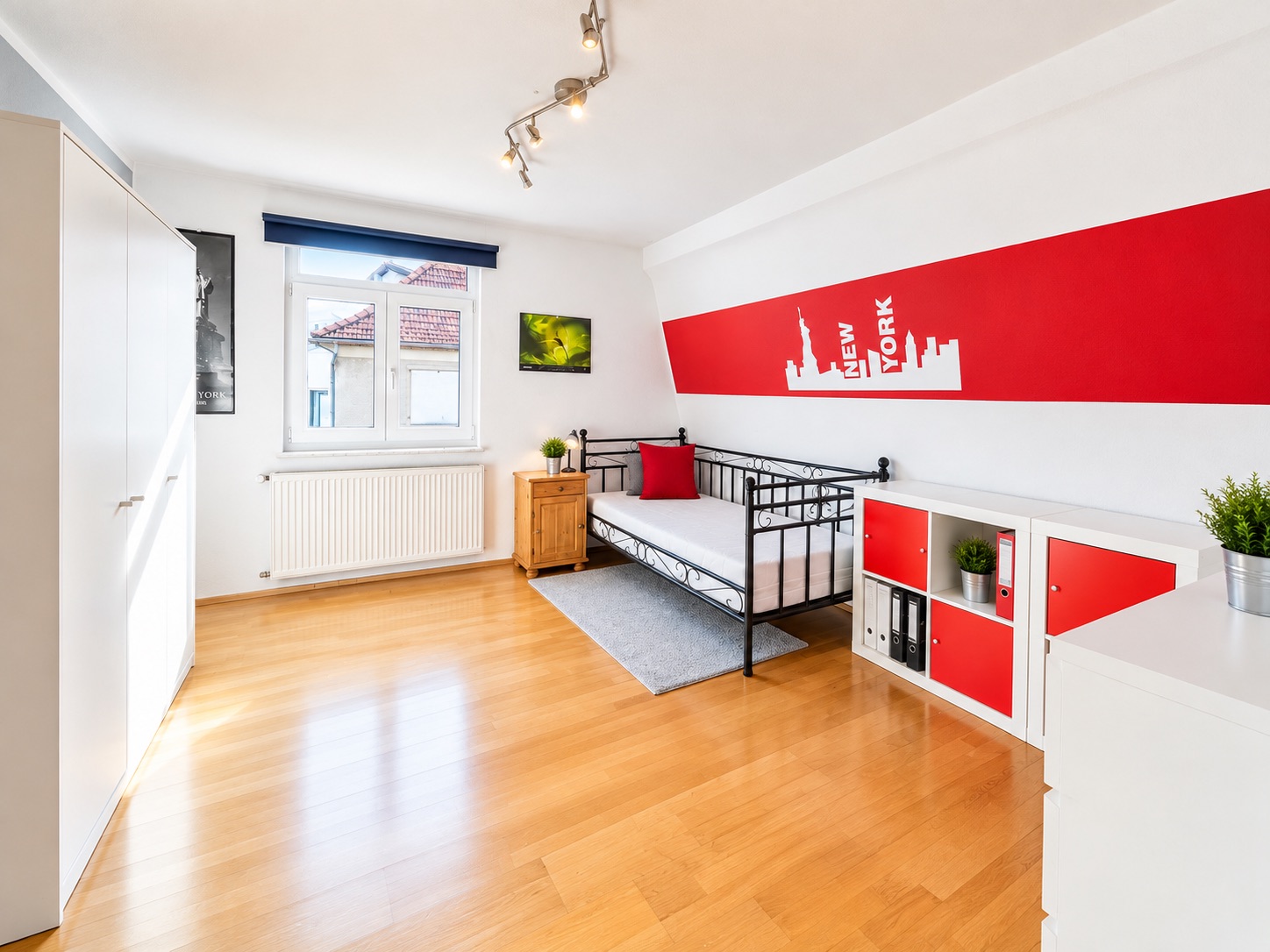 Helles Zimmer mit Einzelbett, Schrank, Regal, Holzboden und Wandbild mit New York Motiv.