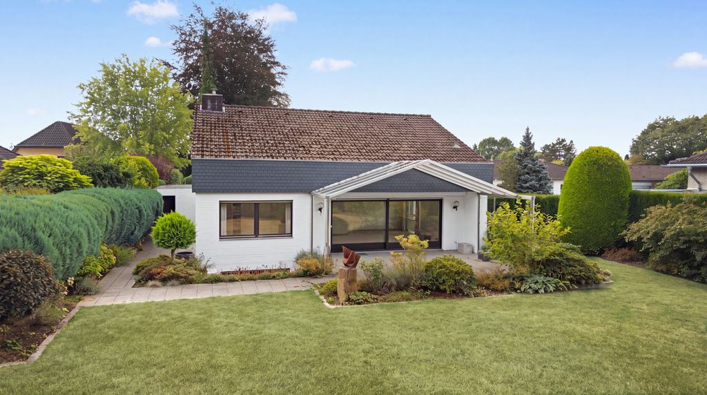 Einfamilienhaus mit Satteldach, großen Fenstern und gepflegtem Garten im Vordergrund.