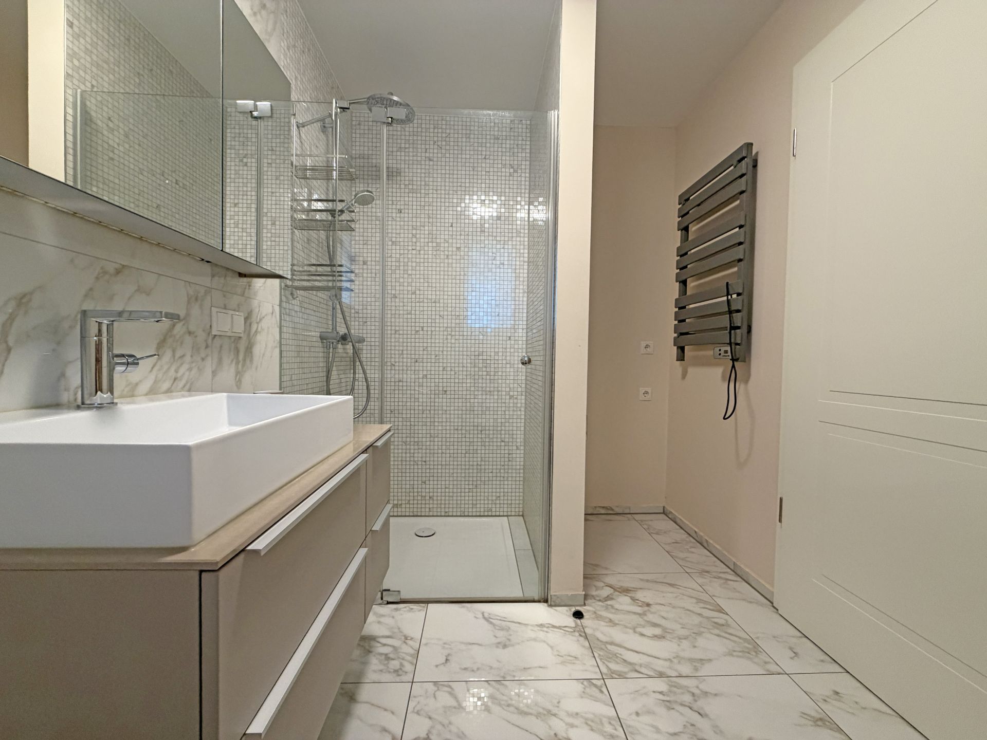 Modernes Bad mit Waschbecken, großer Dusche und Handtuchheizkörper, Fliesenboden in Marmoroptik.