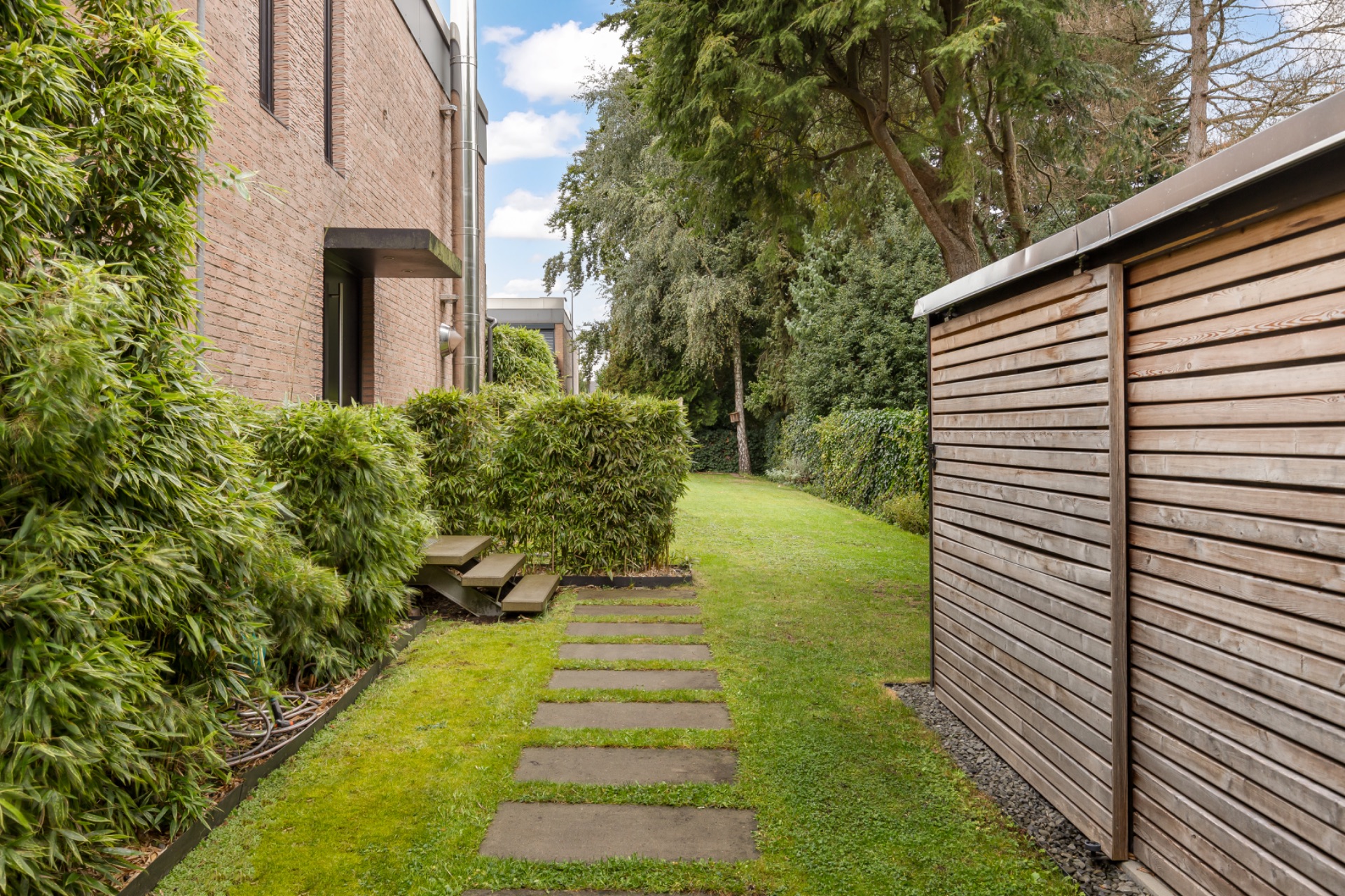 Garten mit Steinplattenweg, Holzzaun und Begrünung neben einem Wohnhaus.