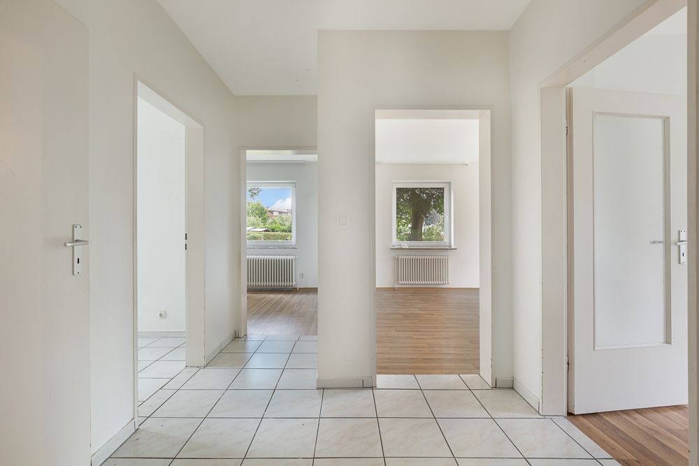 Heller Flur mit weißen Wänden, Fliesenboden und offener Sicht in mehrere Zimmer mit Fenstern.