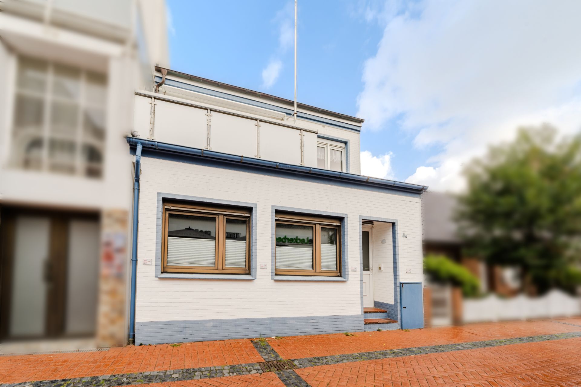 Zweistöckiges weißes Wohnhaus mit blauen Akzenten und drei Fenstern im Erdgeschoss.