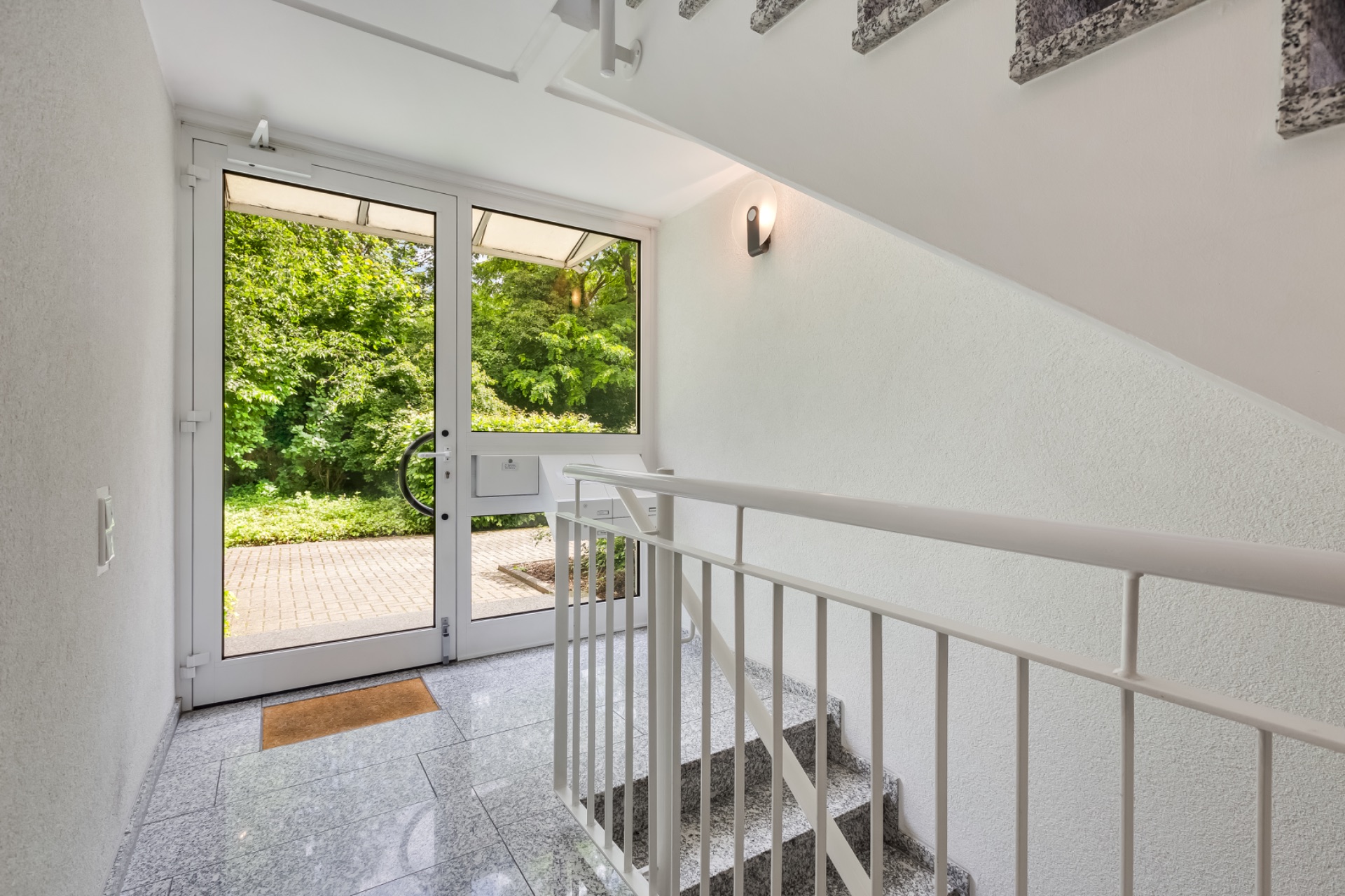 Heller Hausflur mit Glastür, Blick nach draußen auf Garten und Weg.