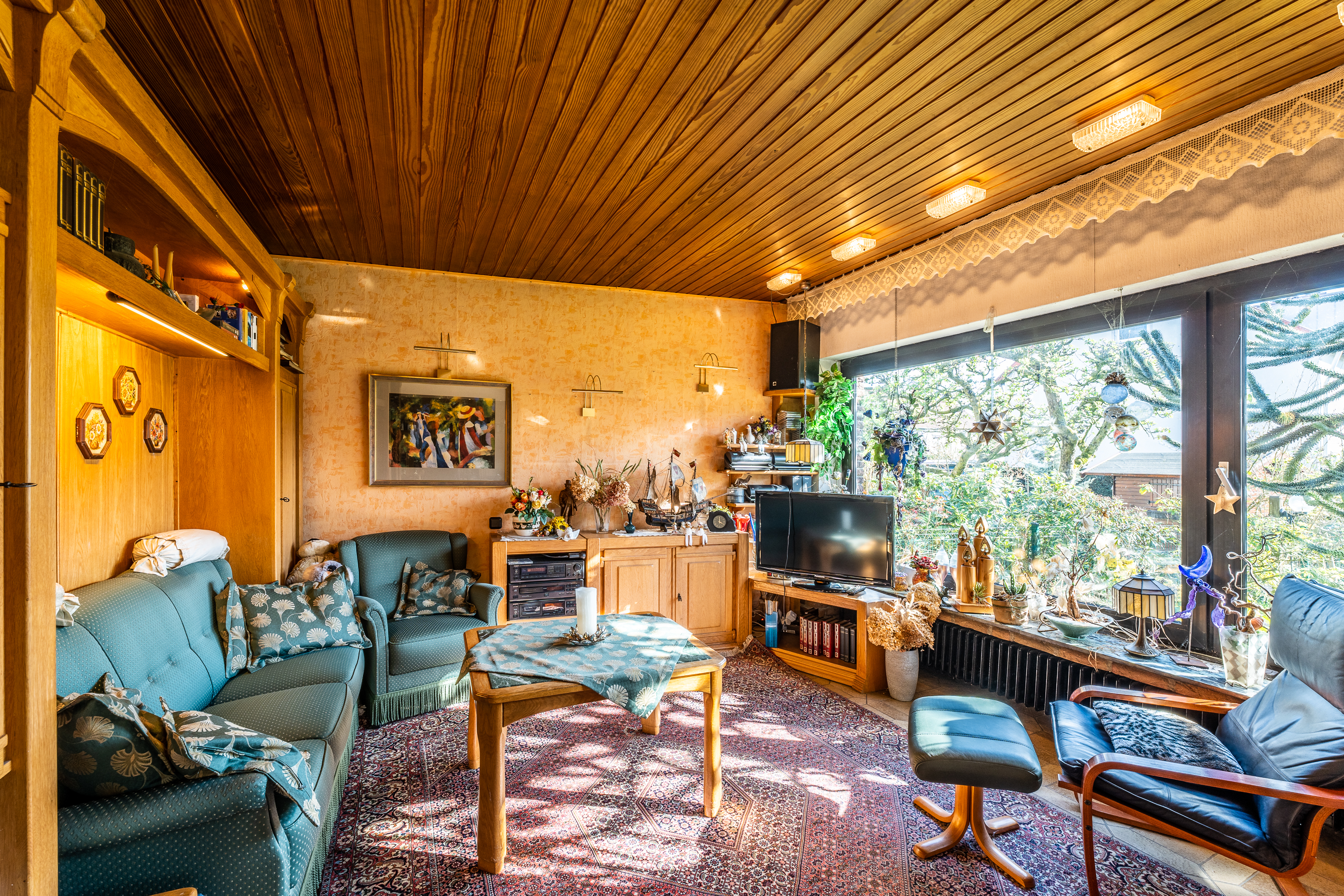 Gemütliches Wohnzimmer mit Sofa, Sesseln, Teppich, großem Fenster und vielen Dekorationen.