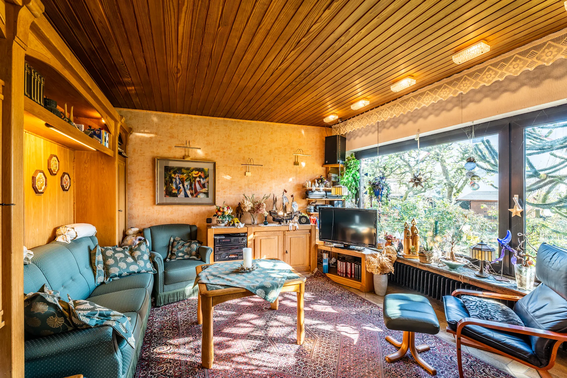 Gemütliches Wohnzimmer mit Sofa, Sesseln, Teppich, großem Fenster und vielen Dekorationen.